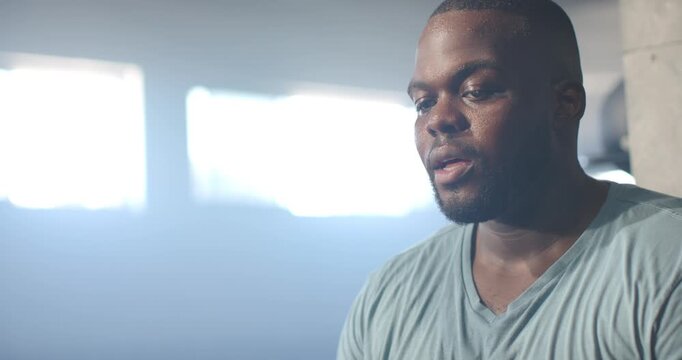 African American man in V-neck tee sweating gasping turning to camera by gym windows, copy space