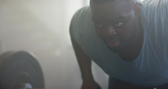African American man gripping barbell, pulling weight in gym wearing gray shirt gaining strength
