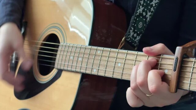 Playing acoustic guitar with a capo while strumming and creating a steady rhythm
