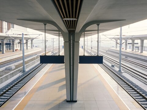 Modern train station platform with a distinct overhead concrete canopy and parallel railway tracks Long shadows fall across the clean tiled floor