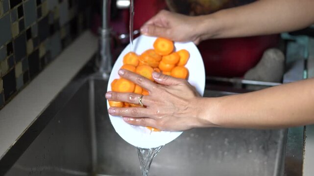 Hands Washing Sliced Carrots Under Running Water in Kitchen Sink