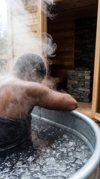 Ice bath therapy scene featuring an African American man immersed in a tub with steam rising, set outdoors in a wooden sauna. The image captures relaxation and wellness. Image made using Generative AI