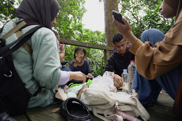 Asian Muslim mother having a picnic lunch with her son and daughter in the middle of the forest, family bonding