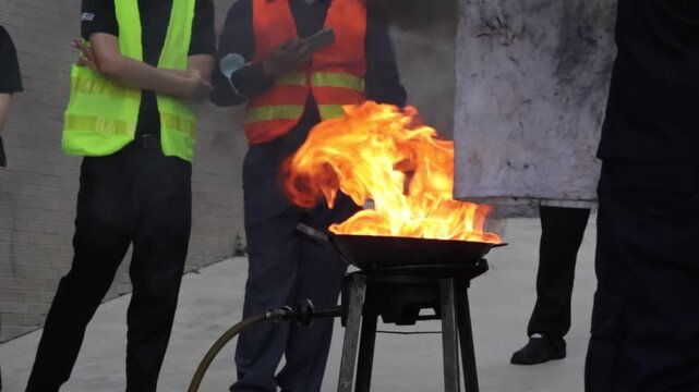 Fire flame fire extinguisher safety training drill with firefighter emergency response, controlled pan fire and smoke outdoor workplace demonstration