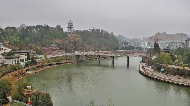 Wide aerial shot of Tuojiang River in Jianyang, Sichuan. Features a bridge with traffic, a traditional pagoda on the hill, and modern residential buildings under an overcast sky. 1080p.