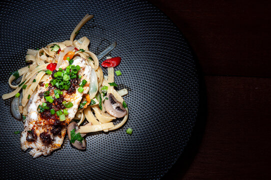 Spagetti aglio olio z oliwą z oliwek na czarnym talerzu stojącym na stole