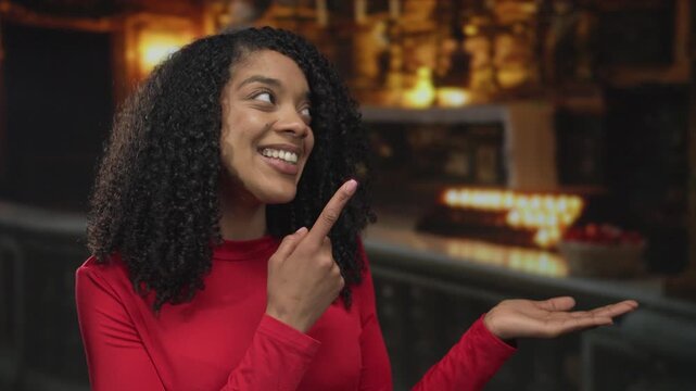 African american woman smiles broadly and points finger to palm in a church building illuminated by candlelight; warm welcome.