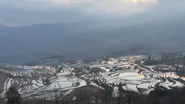 Breathtaking aerial view of the Honghe Hani Rice Terraces in Yunnan, China. The flooded terraces reflect the morning light against misty mountains. UNESCO World Heritage Site.