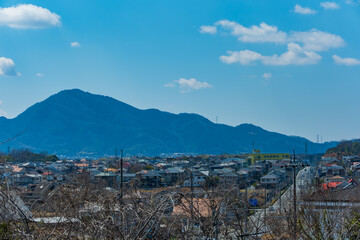 日本の青空と雲の下に広がる山並みと穏やかな住宅街の街並み
