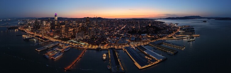 Fototapeta premium San Francisco downtown skyline and Embarcadero waterfront at blue hour, Bay Bridge and Ferry Building aerial view. g.