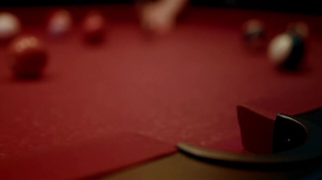 Close-up of a red billiard table with balls and a cue stick in motion