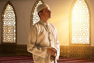 Portrait of young asian muslim man holding rosary beads in the mosque window arch,  eid adha mubarak concept