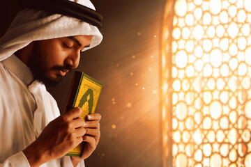 Young asian muslim man with beard holding holy book quran in the mosque window arch, eid adha mubarak concept