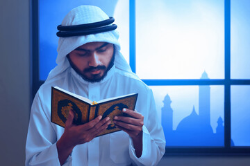 Young asian muslim man with beard reading holy book quran near window at home, eid adha mubarak concept