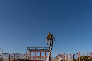 Freerunner moving across a narrow railing in an elevated red metal structure, demonstrating precision and calm over height under clear sky. Precision in urban acrobatic movement. Parkour performance