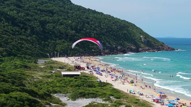 Powered paraglider flying above coastline near Praia dos Ingleses, aerial tracking follow, Santa Catarina Florianopolis Brazil