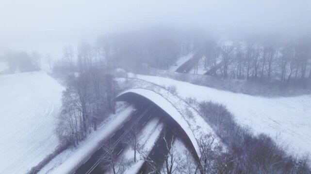 Aerial approach of contrasting Dutch snow landscape with environment nature reserve infrastructure ecoduct in hazy winter conditions