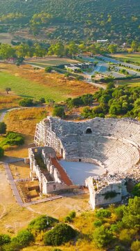 Vertical video. Gelemis, Turkey. Patara Ancient Theatre with 6000 capacity on Kursunlu Hill, monumental roman structure in summer morning. Aerial View, MasterShots, Spiral forward. Rich colors