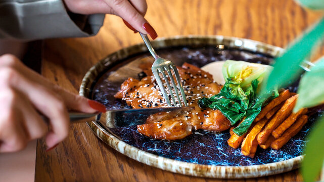 Detailed close-up of hands cutting a gourmet meat dish garnished with pak choi and batata, highlighting texture, craftsmanship, and the sensory experience of fine restaurant dining. Delicious food.