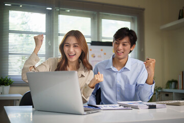 Obraz premium Happy business colleagues celebrating success while looking at a laptop in a modern office, showing teamwork, achievement, and positive work culture.