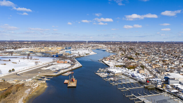 Aerial view of the oceanside waterway and a winter marina with empty boat slips, surrounded by snow covered residential neighborhoods and commercial areas in nassau county, new york