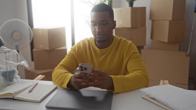Young black man holding smartphone and pumping fist amid cardboard boxes in building; joy new beginnings.
