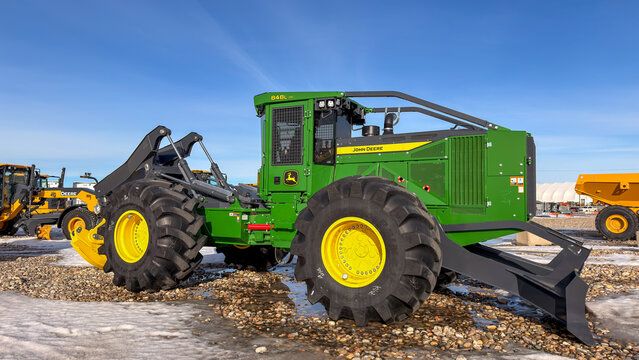 Regina, Canada - February 2026: Green John Deere forestry skidder parked on snowy gravel lot at dealership yard, showcasing heavy logging equipment for timber operations.