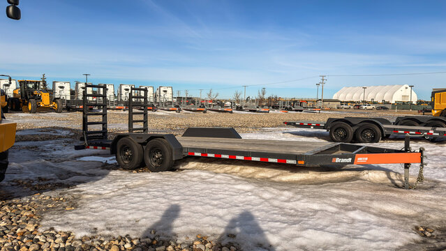 Regina, Canada - February 2026: Brandt flatbed equipment trailer parked on snowy gravel lot at industrial yard, showcasing heavy duty transport solution for construction machinery.