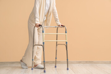 Woman in pajamas with medical walker near beige wall