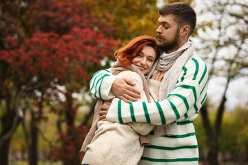 Fototapeta premium Cute young couple in warm sweaters and scarves hugging at autumn park