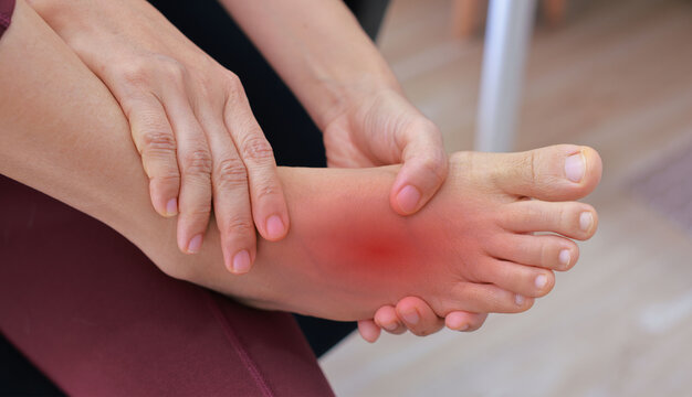 Woman massaging her painful foot with red highlight on sole and instep. Foot pain, plantar fasciitis, muscle strain, gout and peripheral neuropathy concept for health care and physical therapy.