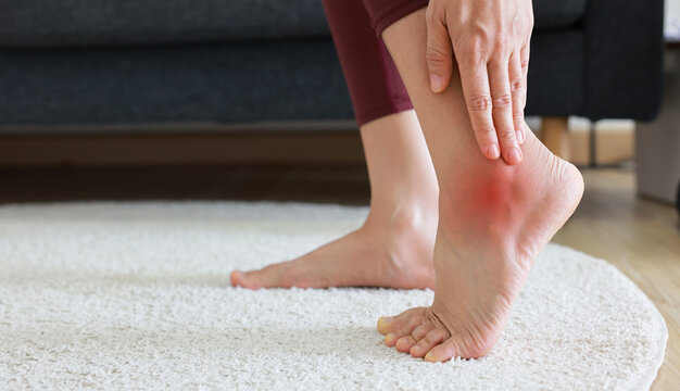 Woman standing and massaging her painful heel with red highlight. Heel spur, plantar fasciitis, Achilles tendonitis and foot injury concept for health care, physical therapy and medical treatment.