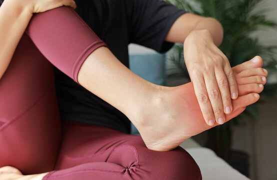 Woman massaging her painful foot with red highlight on sole and instep. Foot pain, plantar fasciitis, muscle strain, gout and peripheral neuropathy concept for health care and physical therapy.