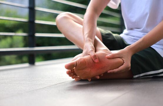 Woman sitting and massaging both of her painful feet with red highlight on soles. Foot pain, plantar fasciitis, overused feet and peripheral neuropathy concept for health care and therapy.
