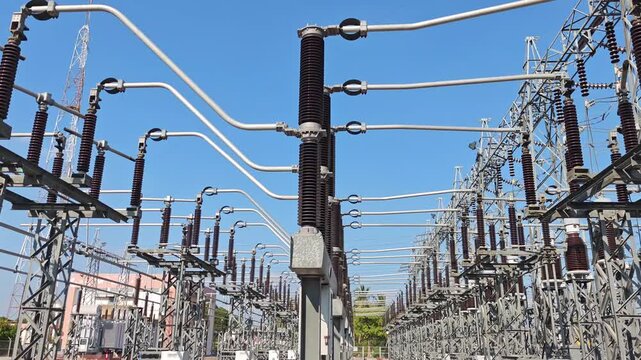 Panning right video view of high voltage electrical power substation switchyard with instrument transformer and disconnect switch equipment on steel structure under blue sky.