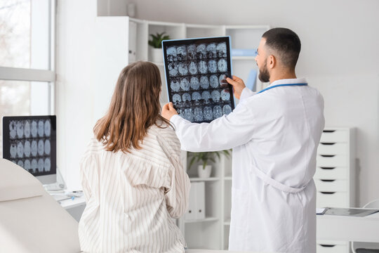Male doctor showing MRI scan of head to woman in clinic, back view