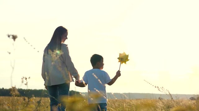 happy family. mother holds child by hand going sunset. son holds hand loving mother. child son boy playing with windmill his hands. pinwheel toy concept. kid with mom park sunset. chidhood dream.