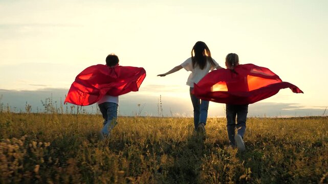 happy family superhero costumes run sunset park. childhood dream defeat evil. play nice guy red cape. childish fantasy. mother girl boy son daughter run. teamwork. family superheroes run help happy