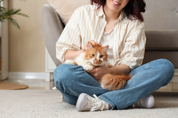 Young woman stroking cute ginger cat on floor at home