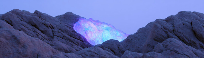 Obraz premium Giant glowing battery core embedded into rocky mountain face at dusk with blue and purple light shining brightly