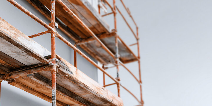 A close-up view of scaffolding attached to a building, conveying the process of construction. The rusty metal structure is against a clear sky
