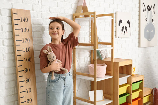 Cute girl with toy measuring height near stadiometer at home