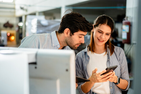 Professional team of printers, man and woman, using a digital tablet and modern equipment for quality control and workflow management in an industrial printing press factory