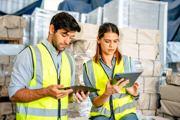 Diverse team of warehouse supervisors in safety vests using digital tablets to manage inventory and...