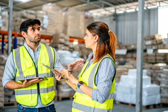Diverse team of warehouse supervisors in safety vests using digital tablets to manage inventory and logistics in a large industrial printing facility storage area
