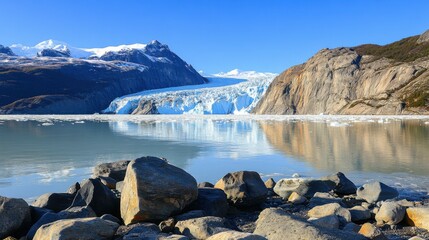 Obraz premium A majestic vast arctic glacier, embraced by towering mountains, spectacularly meets a tranquil blue lake, creating a stunning reflection of the clear sky and surrounding serene landscape.