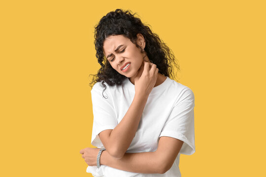 Young African-American woman suffering from skin allergy on yellow background