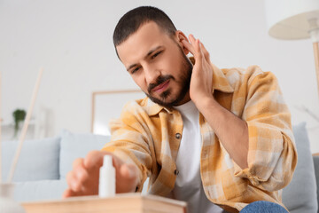Young man with ear pain taking drops from table at home
