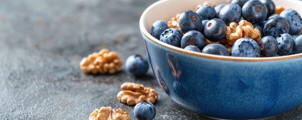 Ceramic bowl filled with ripe blueberries and walnuts on dark surface, nutritious breakfast or snack concept.