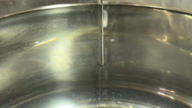 A thin stream of water pours from a faucet into a full stainless steel pot. The continuous flow creates a low murmuring sound as it breaks the surface.